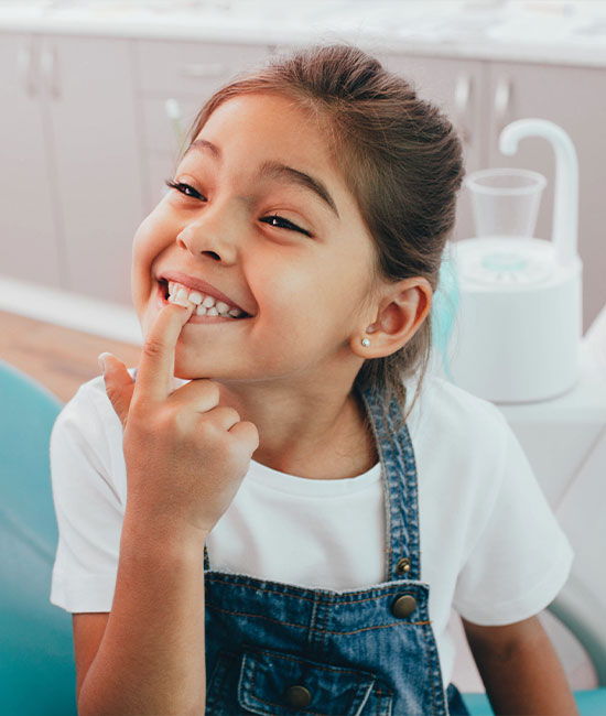 A young girl with a broad smile, looking directly at the camera, while seated in a dentist's chair.