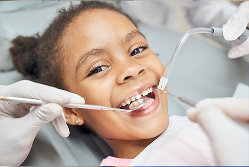 A young child receiving dental care, smiling while sitting in a dentist's chair with medical professionals attending to them.